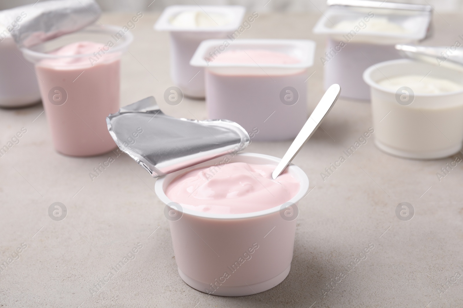 Photo of Plastic cup with fresh yogurt and spoon on grey table