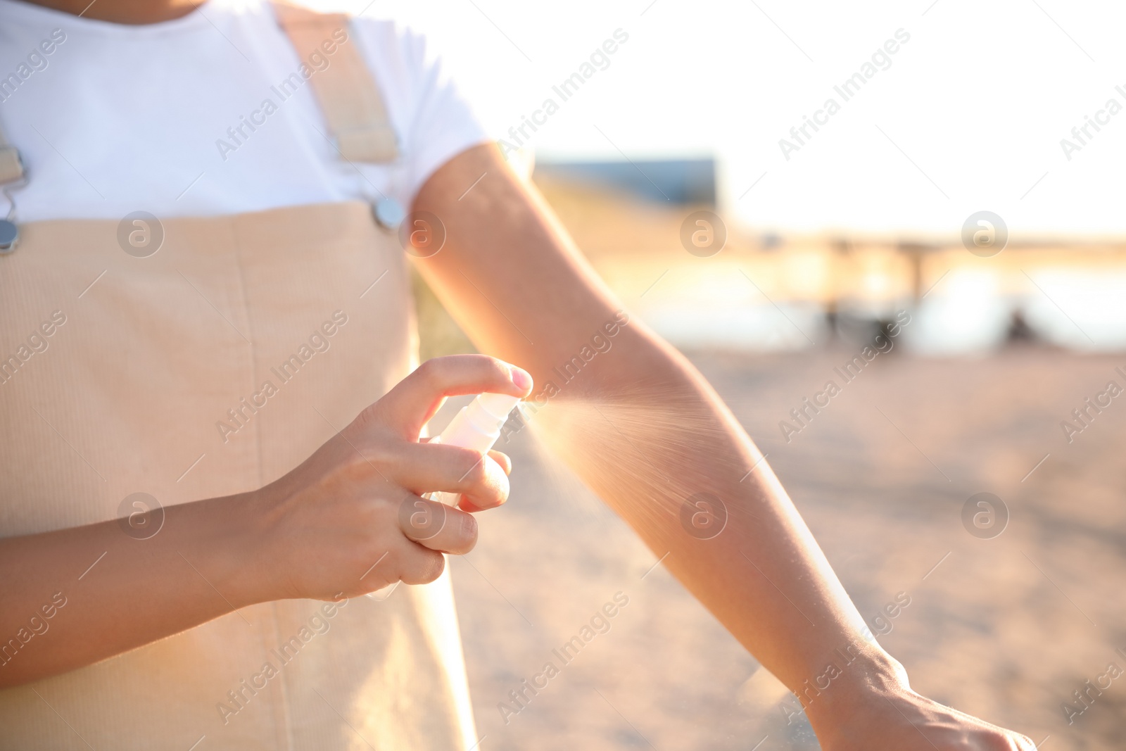 Photo of Young woman using insect repellent on beach, closeup