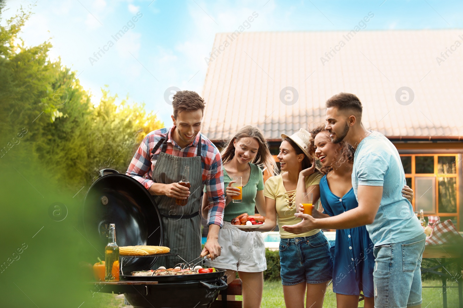 Photo of Group of friends with drinks near barbecue grill outdoors