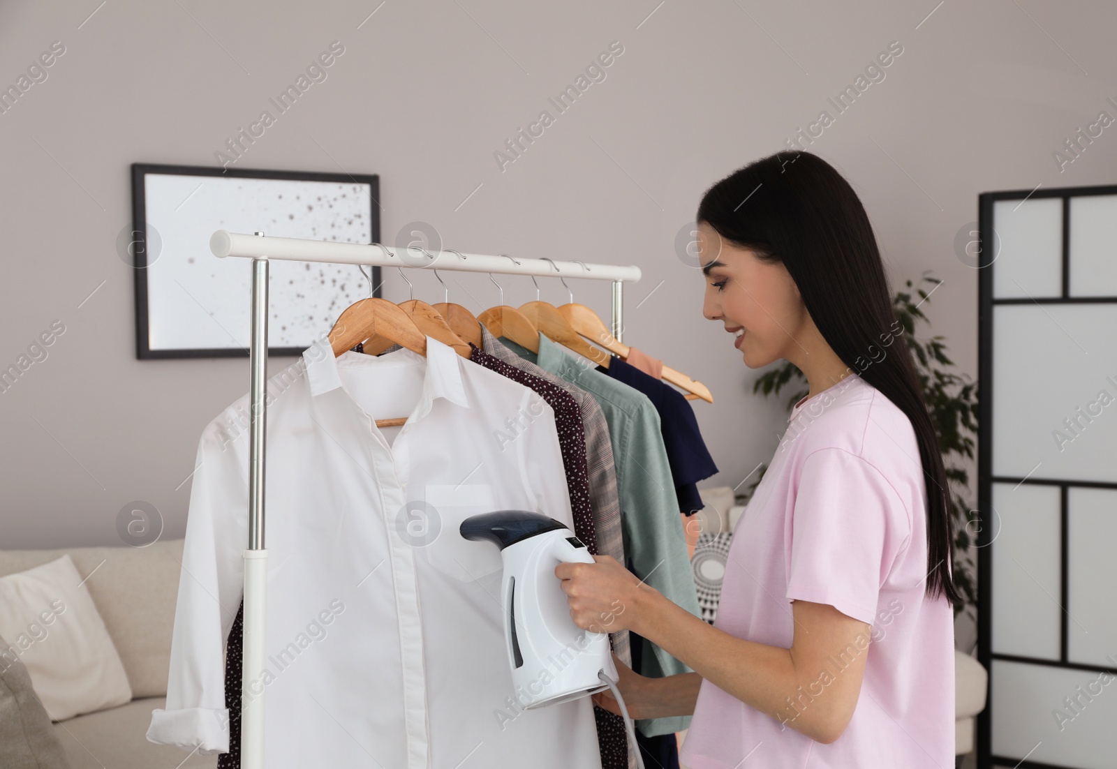 Photo of Woman steaming shirt on hanger at home