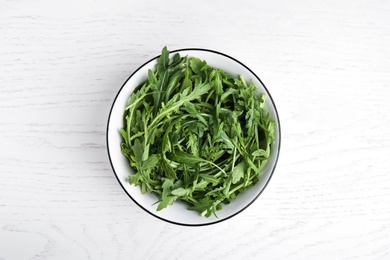 Photo of Fresh arugula in bowl on white wooden table, top view