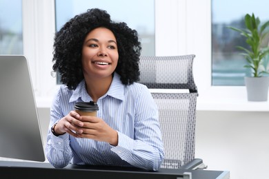 Photo of Young woman with cup of drink working on computer in office