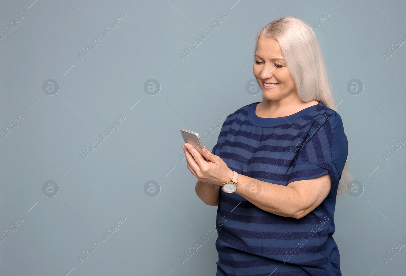 Photo of Mature woman using mobile phone on grey background