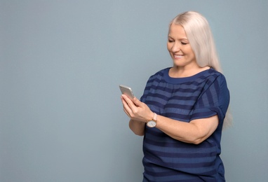 Mature woman using mobile phone on grey background