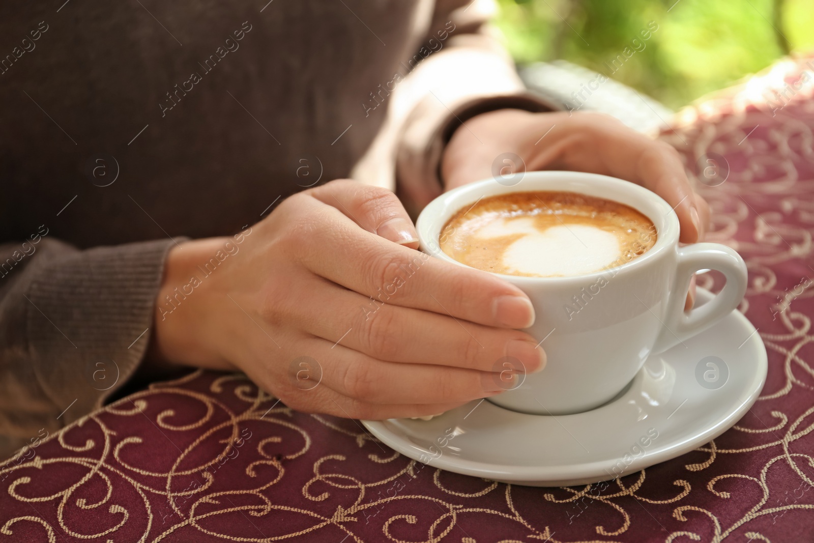 Photo of Young woman with cup of delicious coffee at table