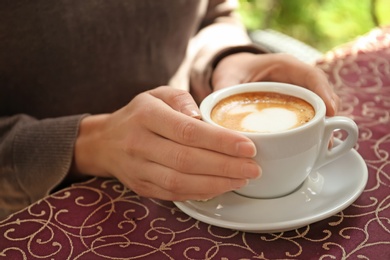 Young woman with cup of delicious coffee at table