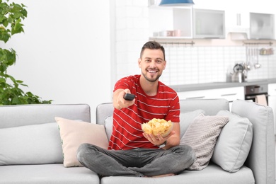 Man with bowl of potato chips watching TV on sofa in living room