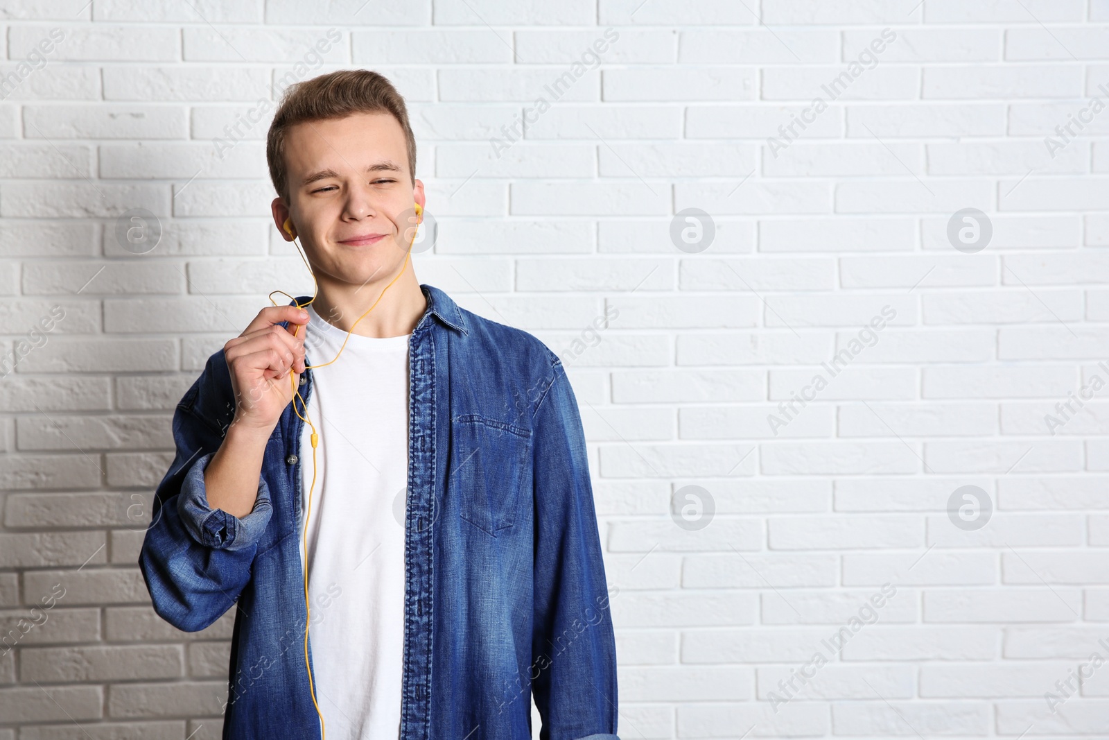 Photo of Teen boy listening to music with headphones near brick wall, space for text