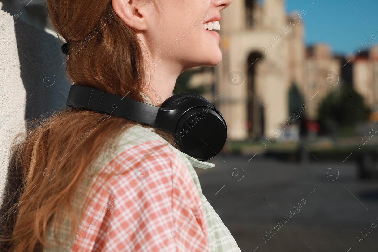 Photo of Smiling woman with headphones outdoors, closeup. Space for text