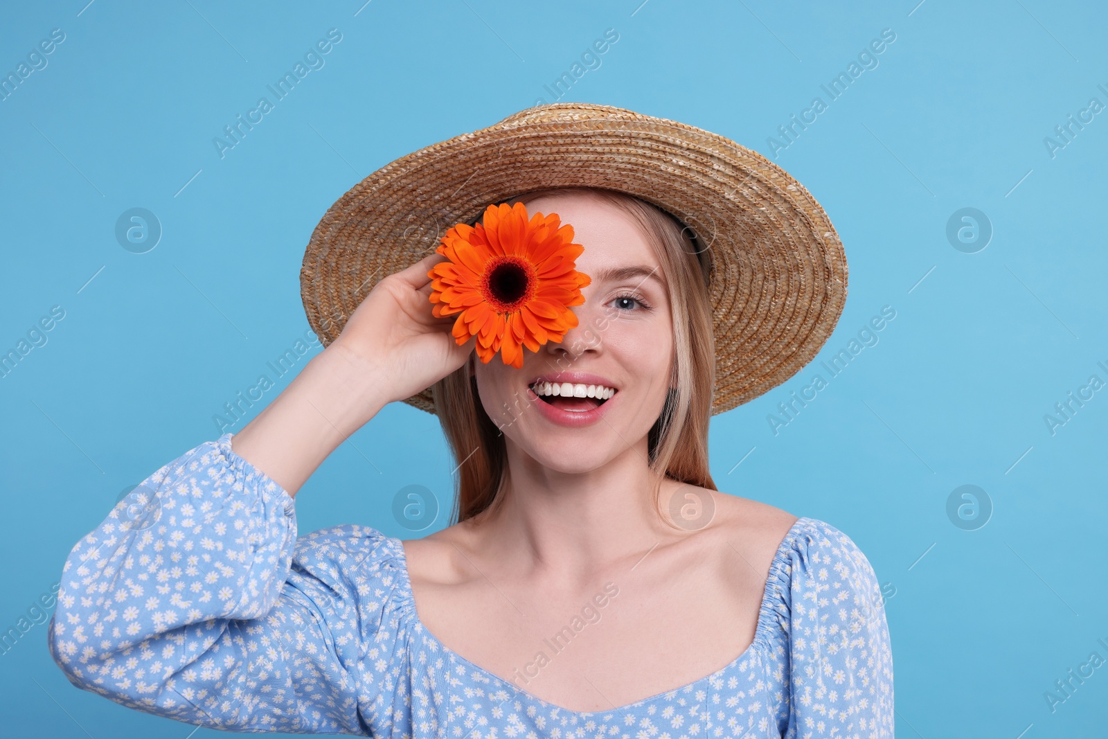 Photo of Beautiful woman with spring flower in hand on light blue background