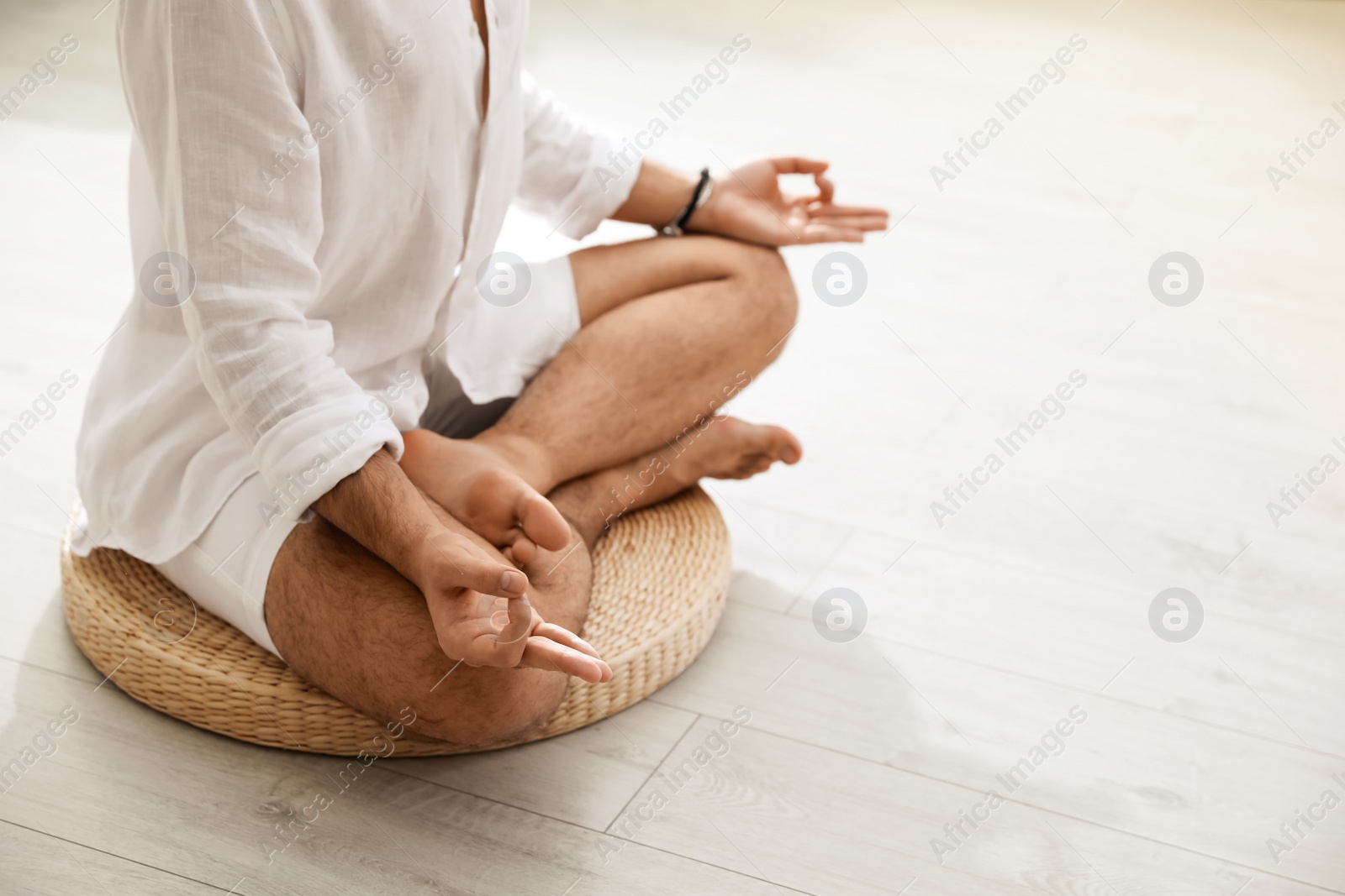 Photo of Young man meditating on straw cushion at home, closeup. Space for text