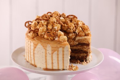 Photo of Caramel drip cake decorated with popcorn and pretzels against light background, closeup