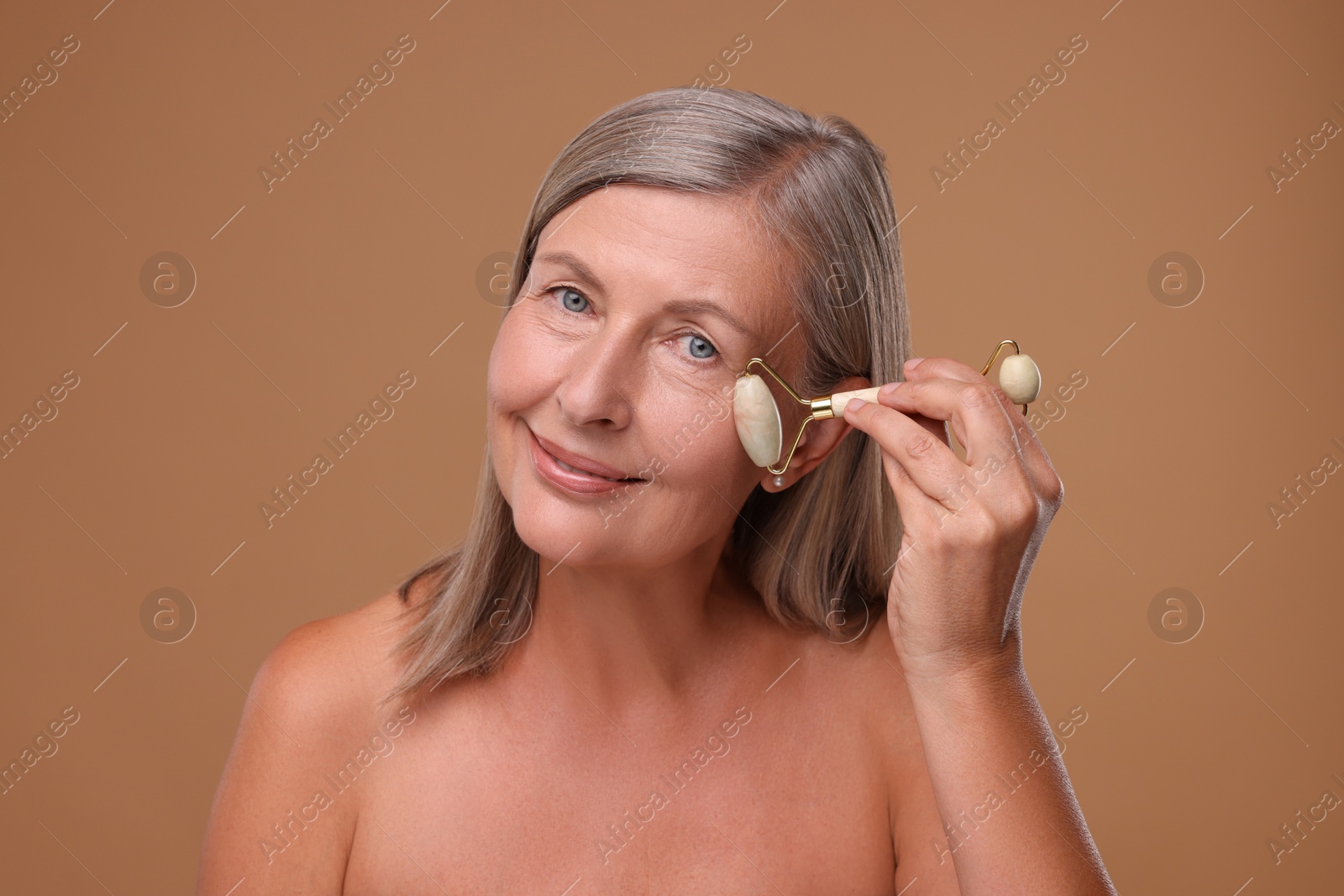 Photo of Woman massaging her face with jade roller on brown background