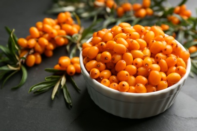 Photo of Fresh ripe sea buckthorn in bowl on black table, closeup