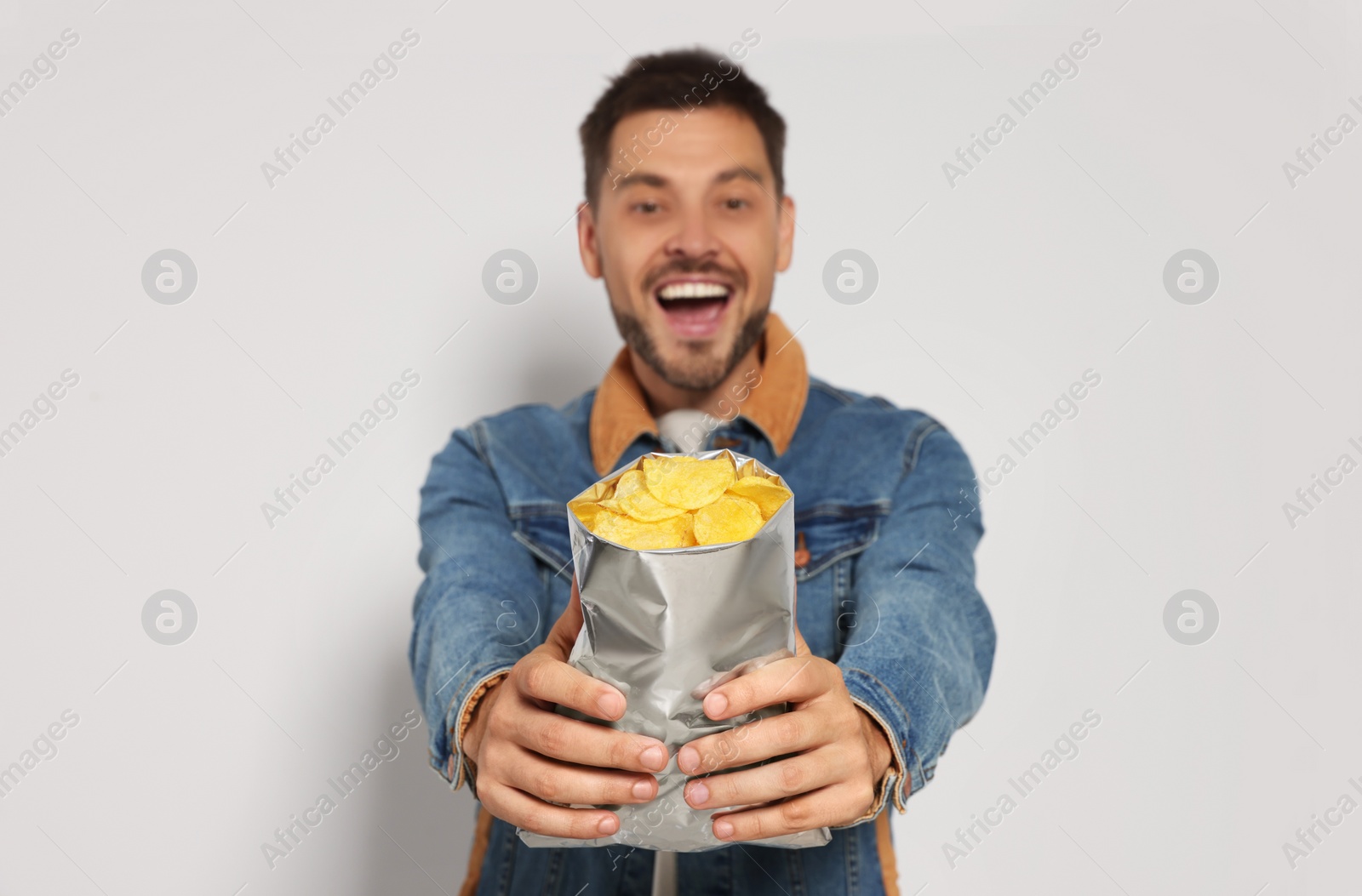 Photo of Handsome man with potato chips against light grey background, focus on hands