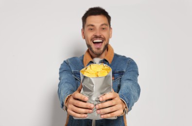 Photo of Handsome man with potato chips against light grey background, focus on hands