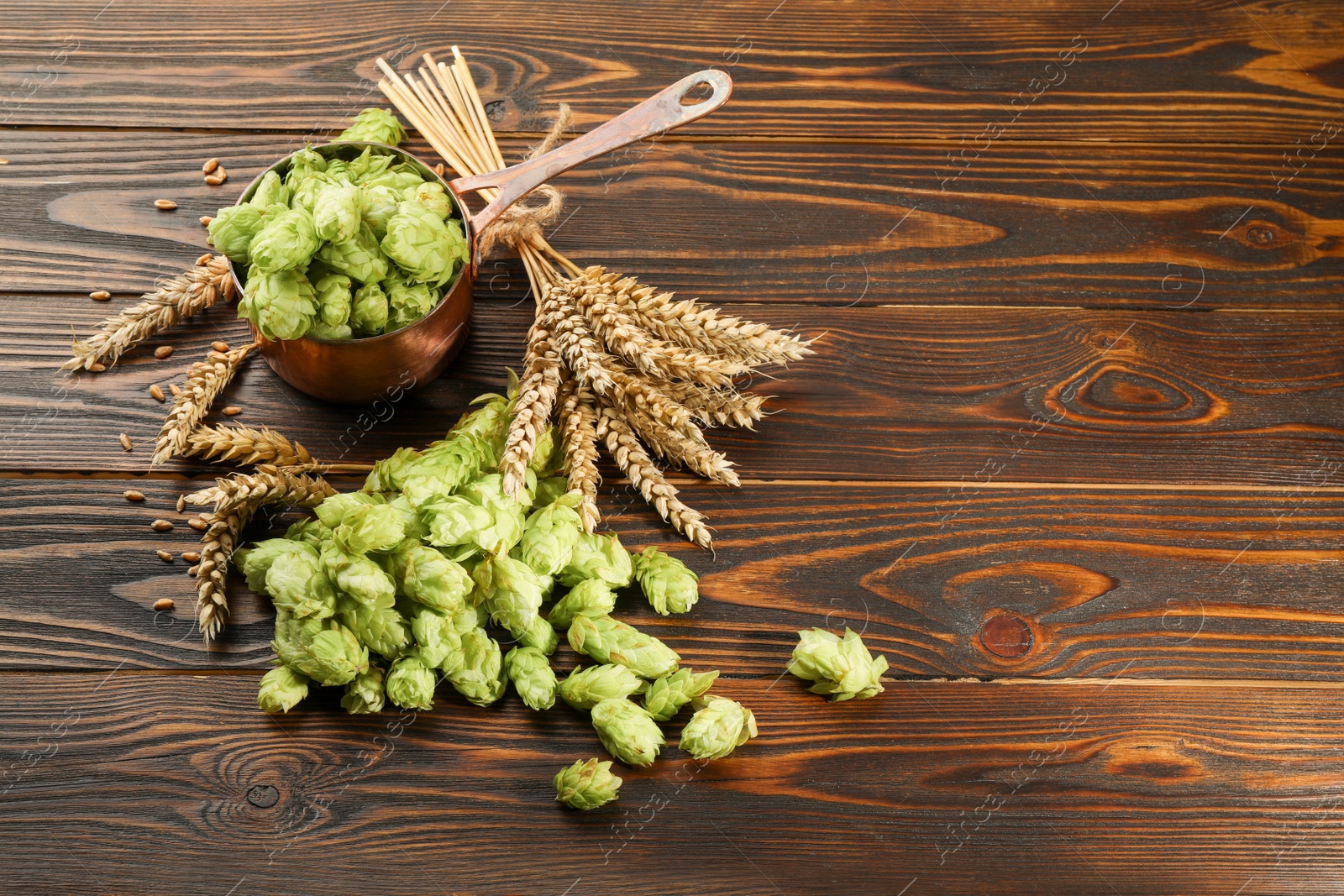 Photo of Fresh hop flowers and wheat ears on wooden table, space for text