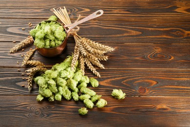 Fresh hop flowers and wheat ears on wooden table, space for text