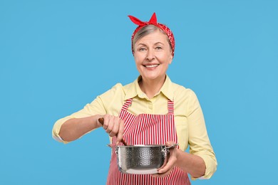 Happy housewife with pot on light blue background