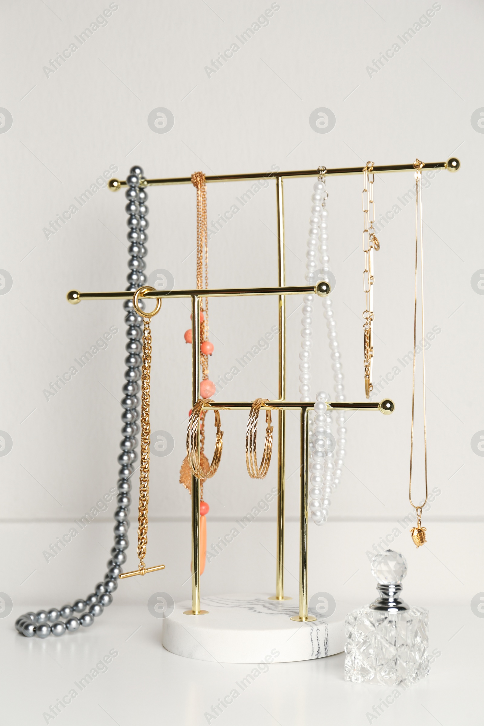 Photo of Holder with set of luxurious jewelry and perfume on white table