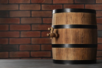 Wooden barrel with tap on table near brick wall, space for text