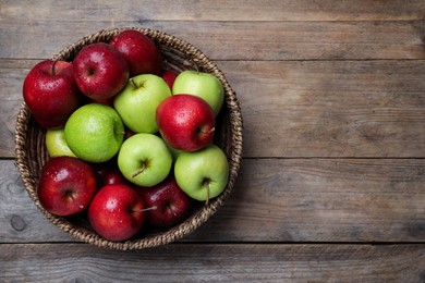 Fresh ripe green and red apples with water drops in wicker bowl on wooden table, top view. Space for text