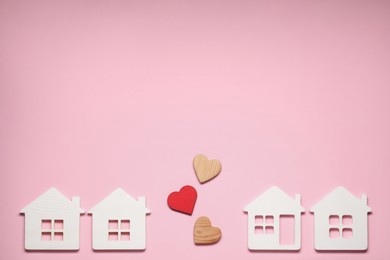 Long-distance relationship concept. Decorative hearts between white house models on pink background, flat lay with space for text
