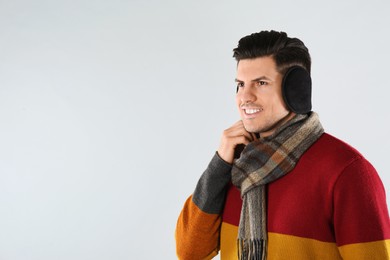 Photo of Man wearing stylish earmuffs and scarf on light background. Space for text