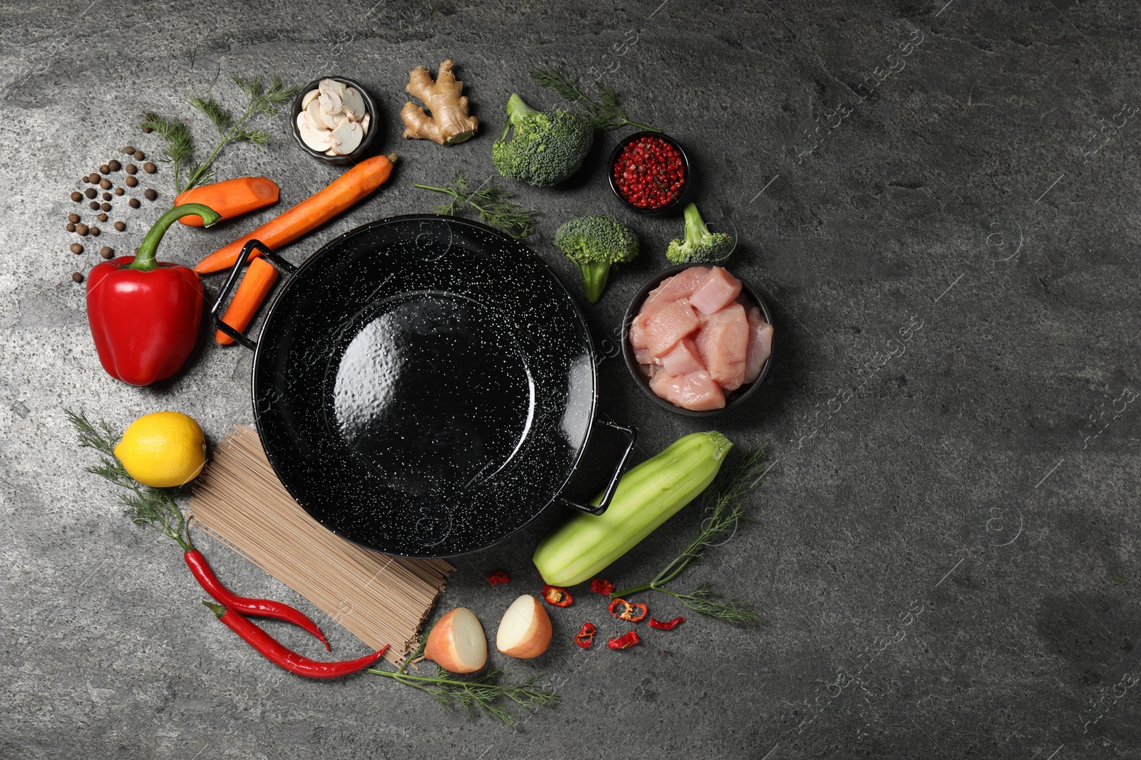 Photo of Empty iron wok surrounded by raw ingredients on grey table, flat lay