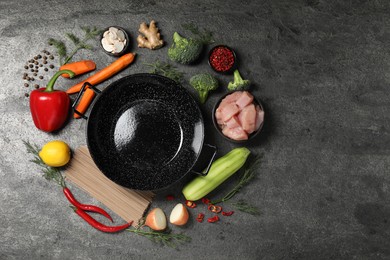 Empty iron wok surrounded by raw ingredients on grey table, flat lay