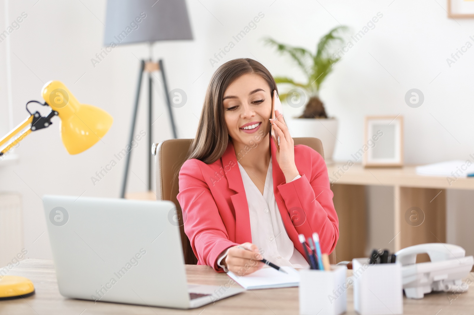 Photo of Young woman talking on phone at workplace