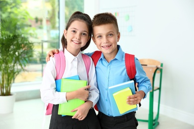 Photo of Cute little children with backpacks and school stationery in classroom