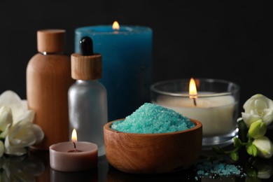 Photo of Beautiful spa composition with different care products, burning candles and flowers on black mirror surface, closeup