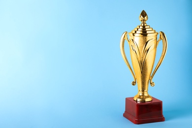 Photo of Golden trophy cup on blue background. Space for text