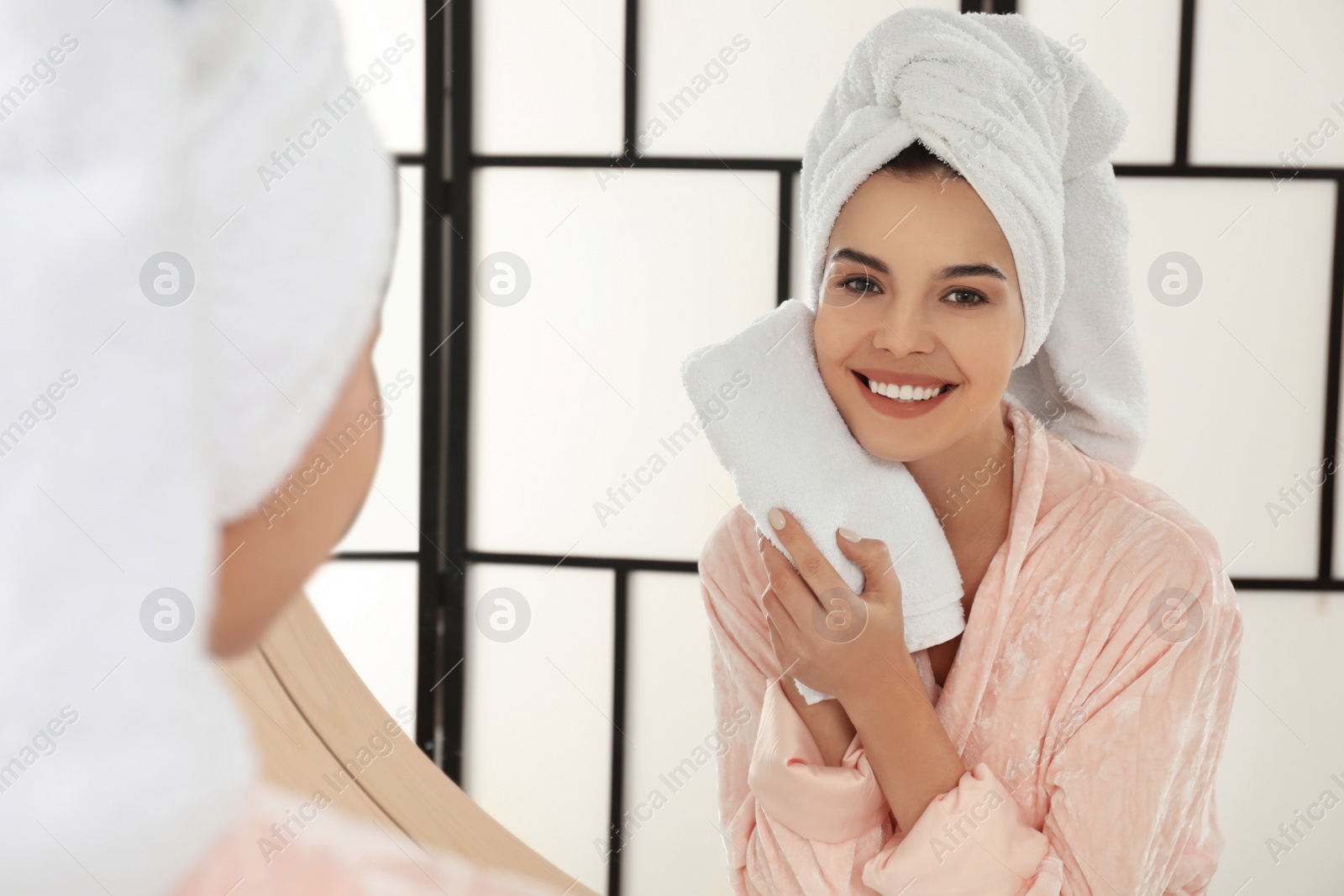 Photo of Young woman wiping face with towel near mirror in bathroom