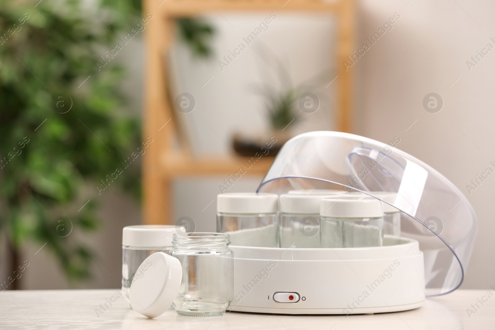 Photo of Modern yogurt maker with empty jars on white table indoors. Space for text