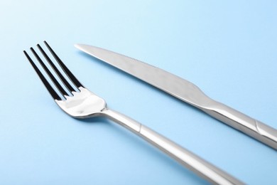 Photo of Stylish cutlery. Silver knife and fork on light blue background, closeup