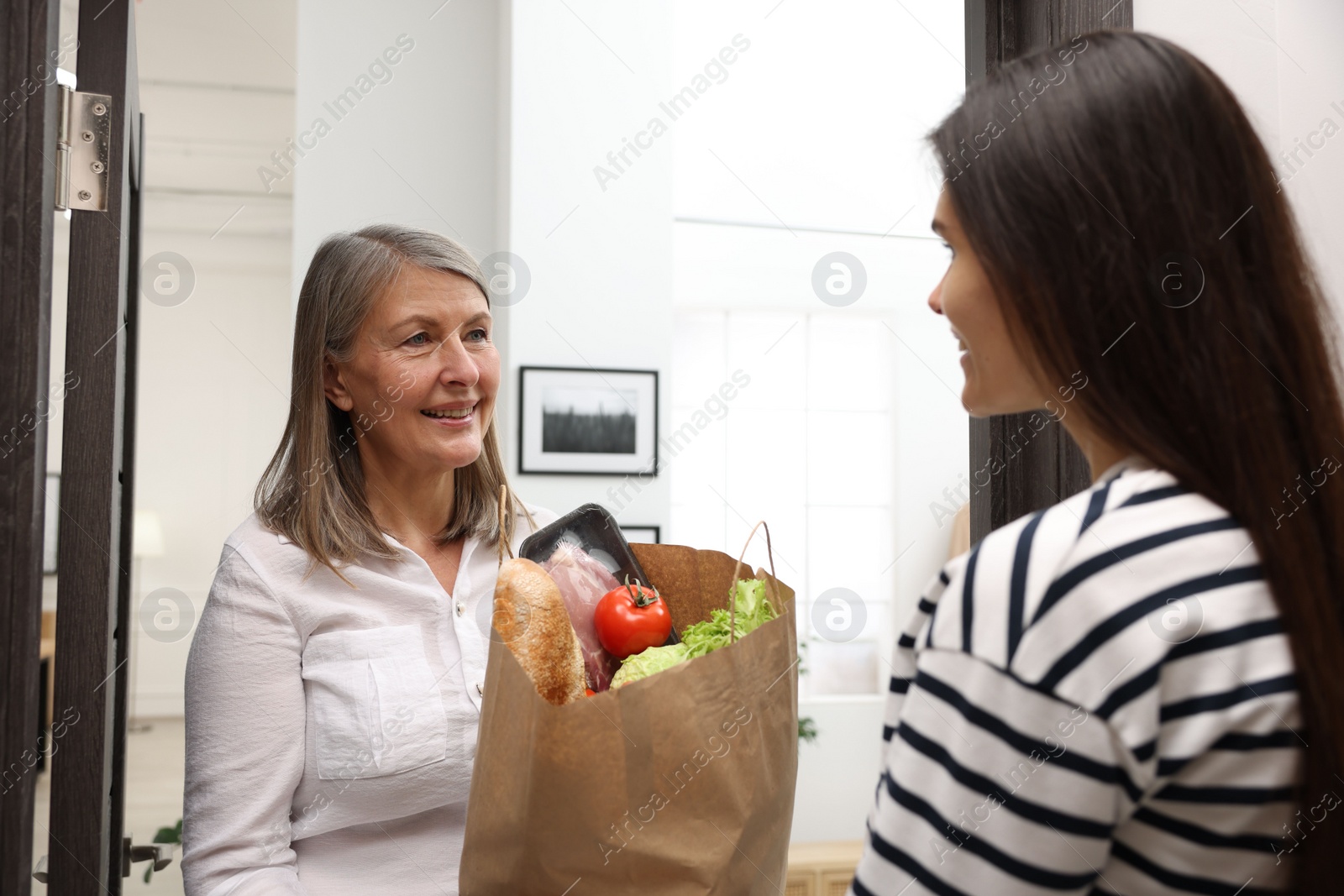 Photo of Courier giving paper bag with food products to senior woman indoors