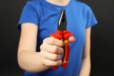 Woman with combination pliers on dark background, closeup