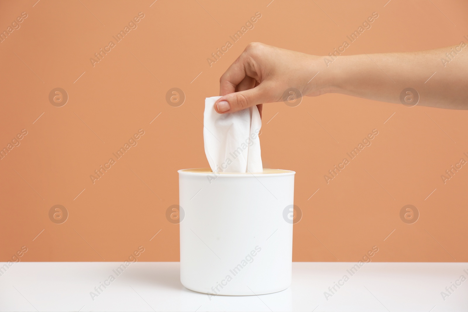 Photo of Woman taking paper tissue from holder on light brown background, closeup