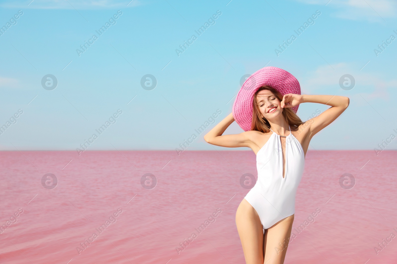 Photo of Beautiful woman in swimsuit posing near pink lake on sunny day