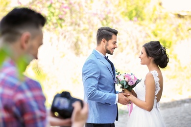 Professional photographer with camera and wedding couple, outdoors