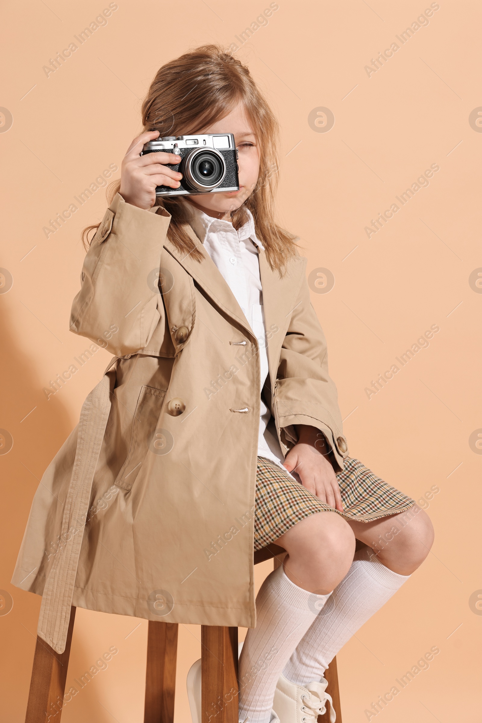 Photo of Fashion concept. Stylish girl with vintage camera on pale orange background