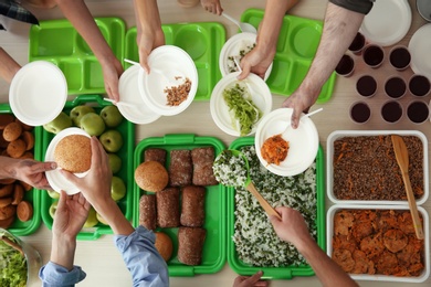 Photo of Volunteers serving food for poor people at table, top view