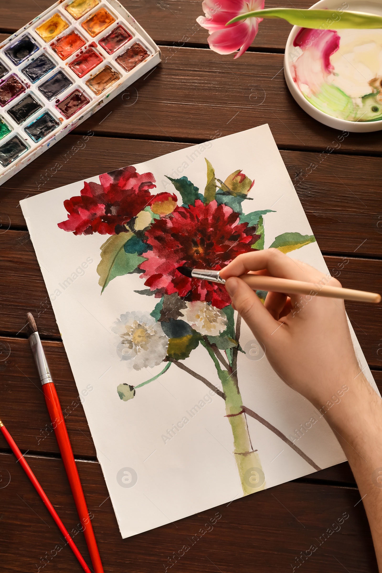 Photo of Woman painting flowers with watercolor at wooden table, top view. Creative artwork