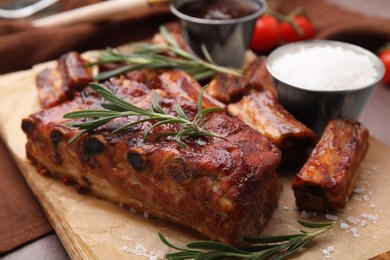 Photo of Tasty roasted pork ribs served with sauce and rosemary on brown table, closeup