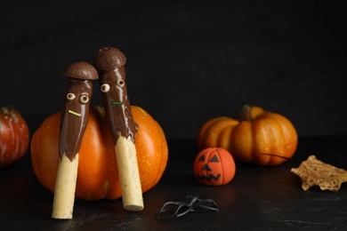 Photo of Delicious sticks with chocolate decorated as monsters on dark background. Halloween treat