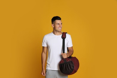 Handsome man with sports bag on yellow background