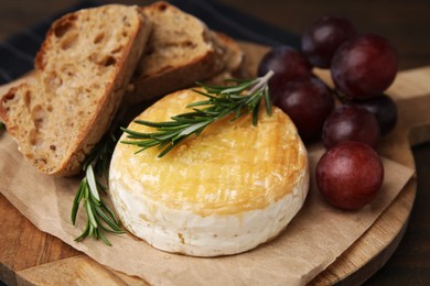 Photo of Tasty baked camembert, pieces of bread, grapes and rosemary on table, closeup