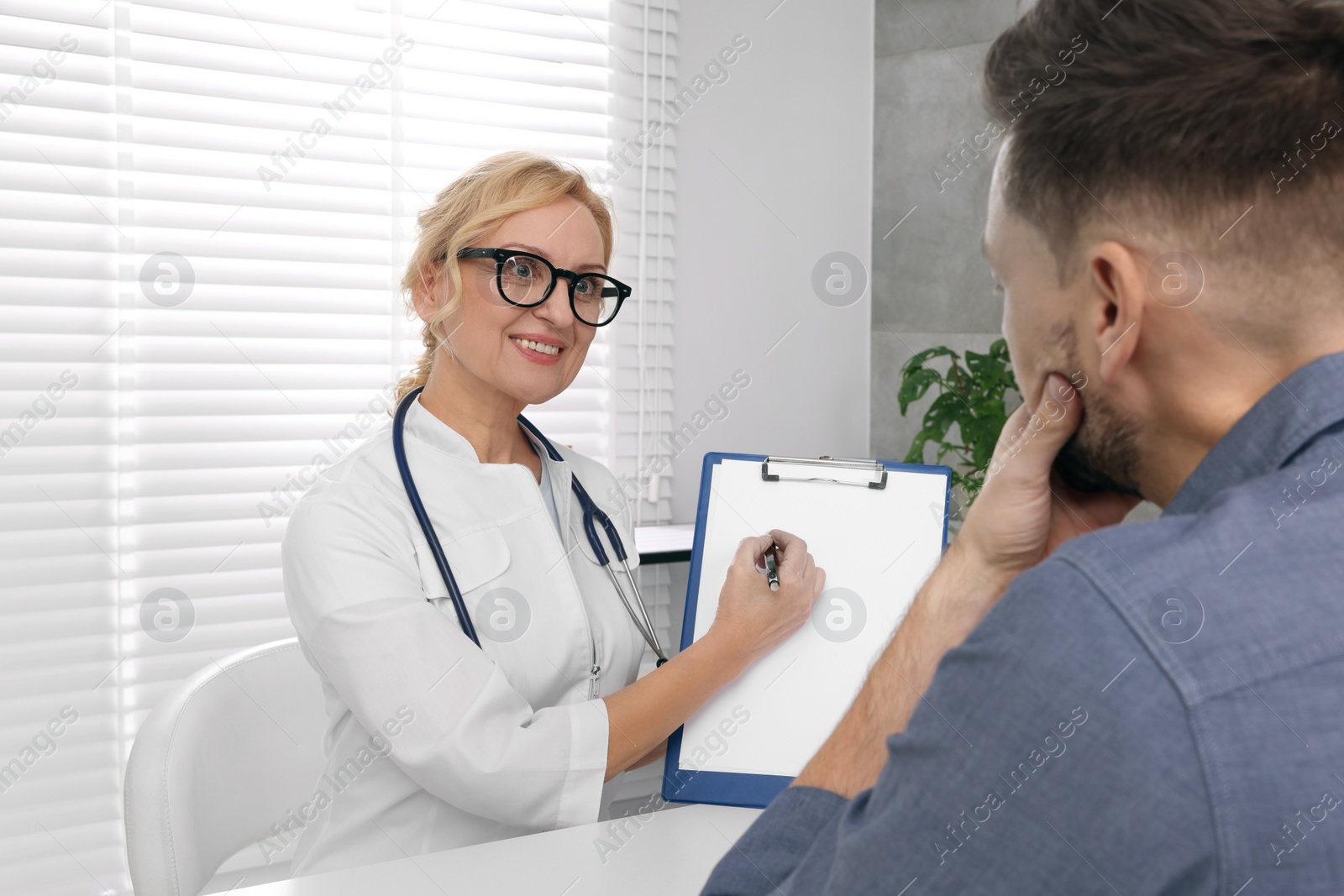 Photo of Doctor with clipboard consulting patient in clinic